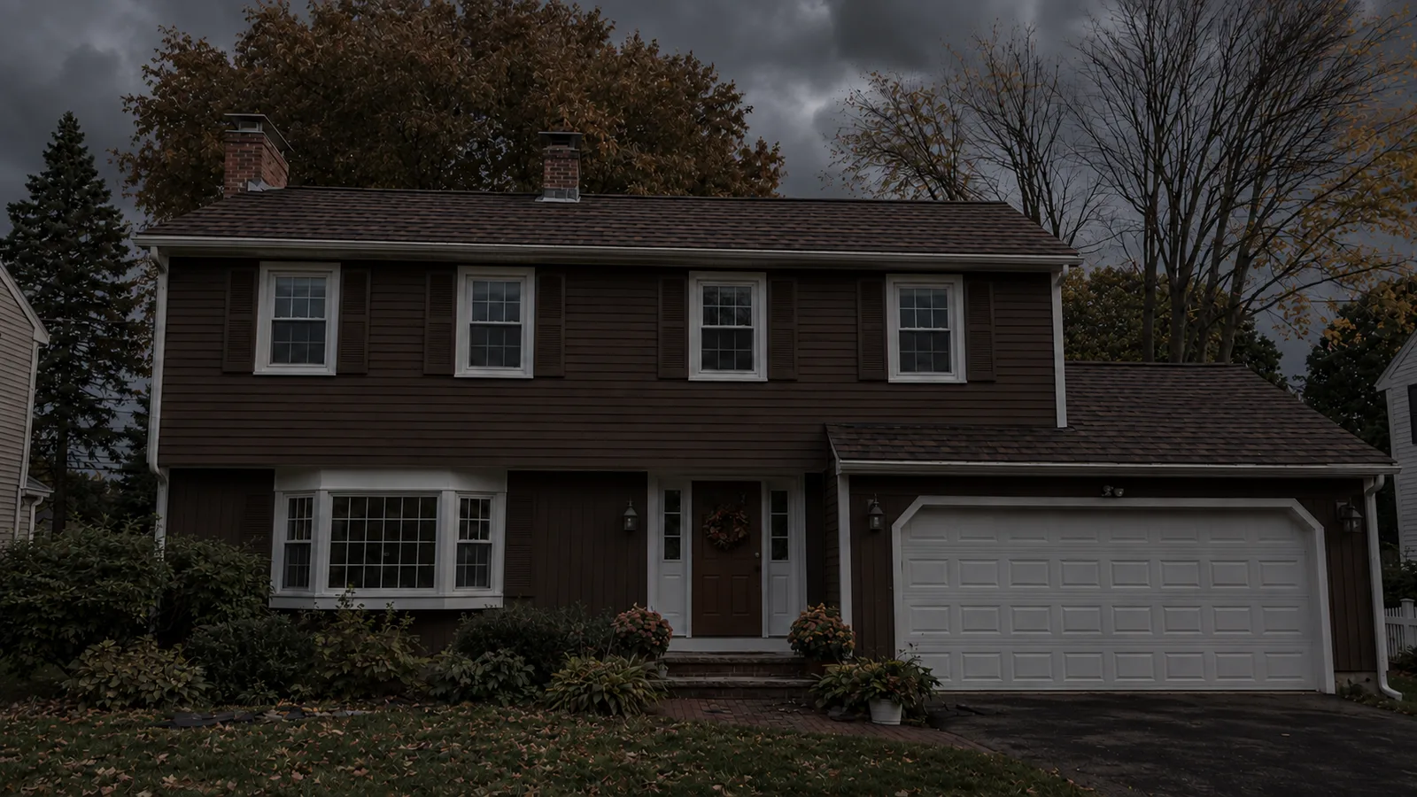 Brown two-story house with continuous brown shingles over the main roof and garage.
